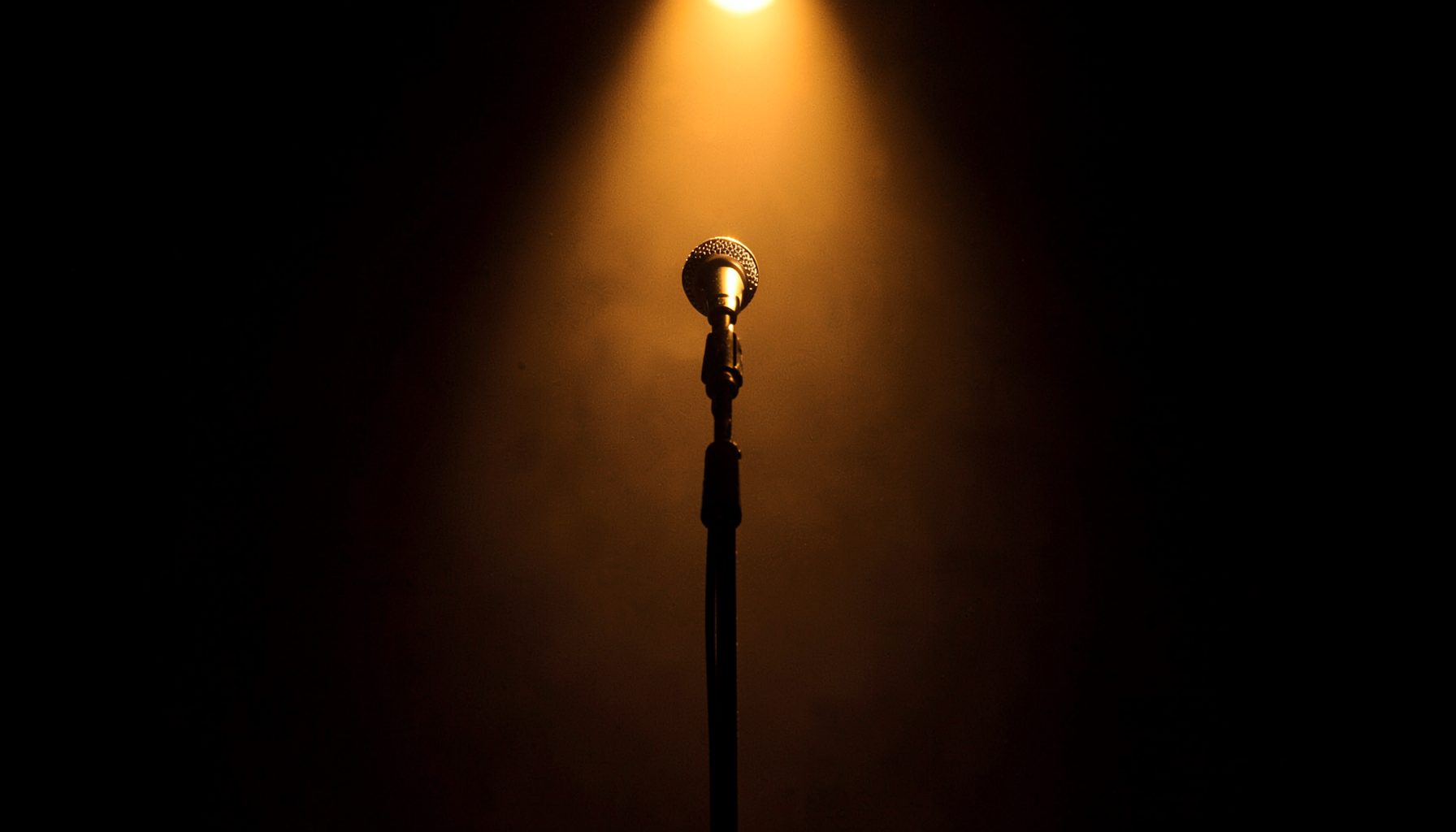 Stage spotlight casting a warm amber glow on an empty microphone stand, theatrical atmosphere