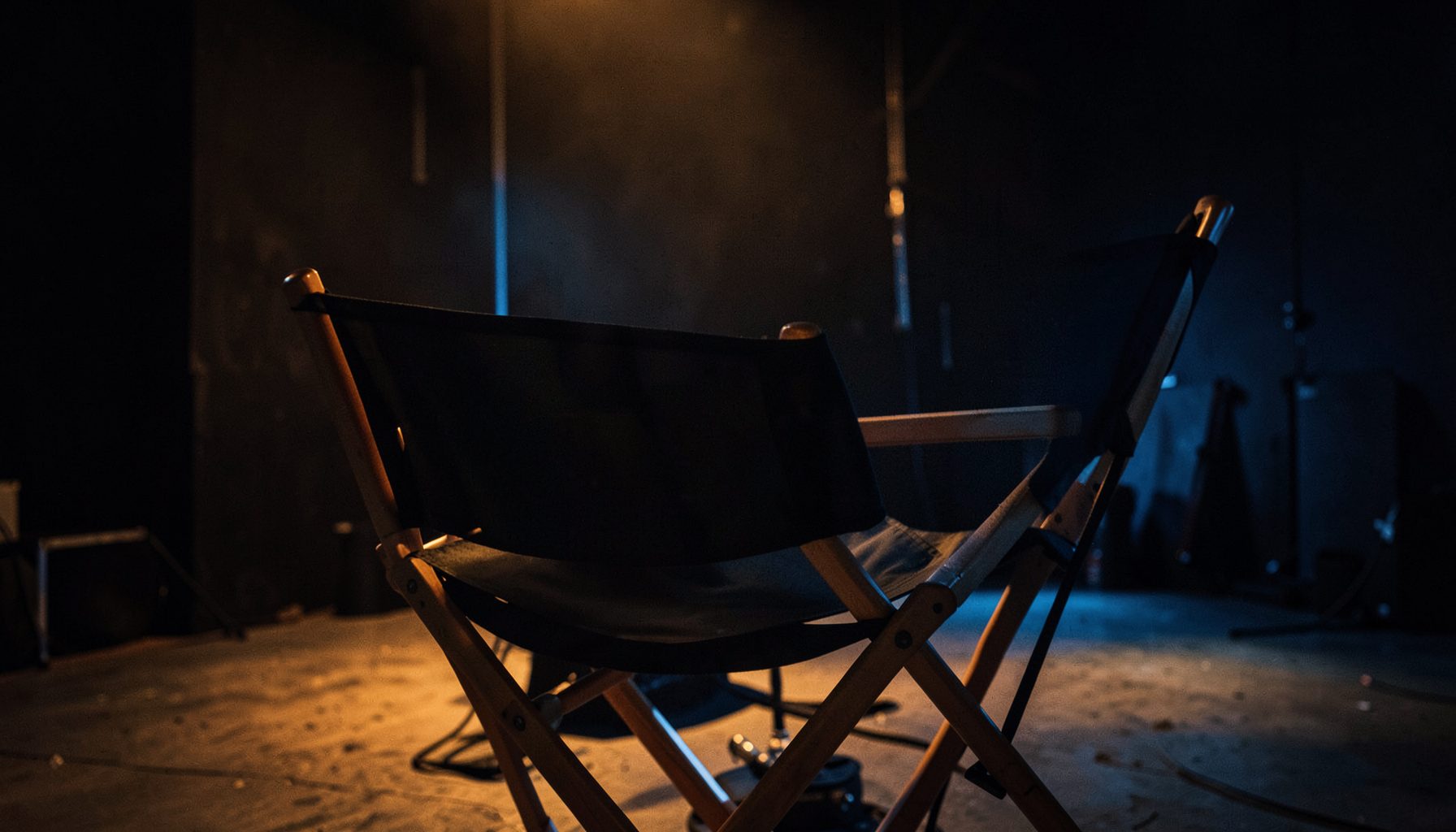 Dimly lit film set with a director's chair in the foreground, warm amber and deep blue tones, cinematic atmosphere
