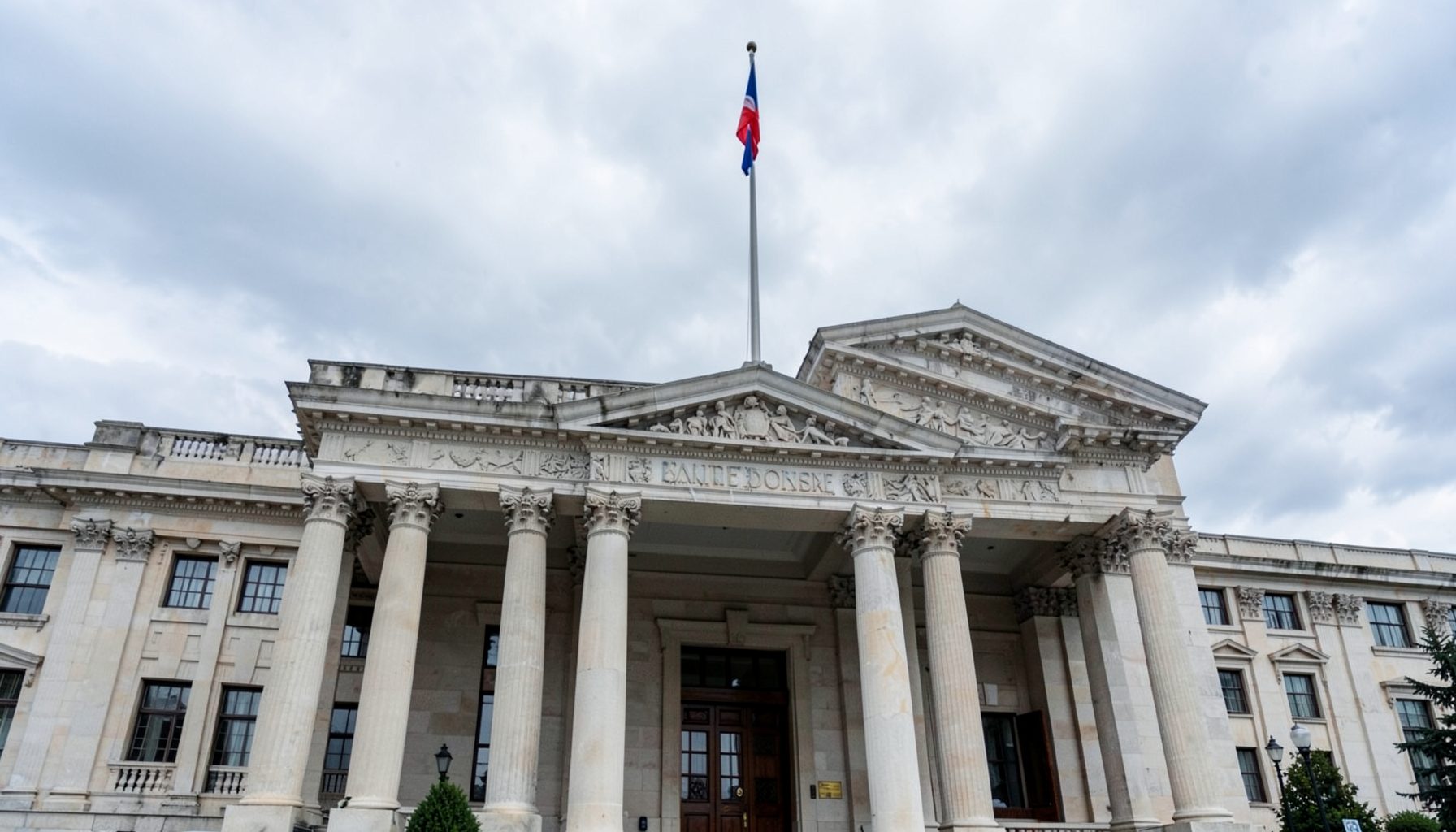 A formal government building facade with columns and a national flag against a cloudy sky, conveying political authority