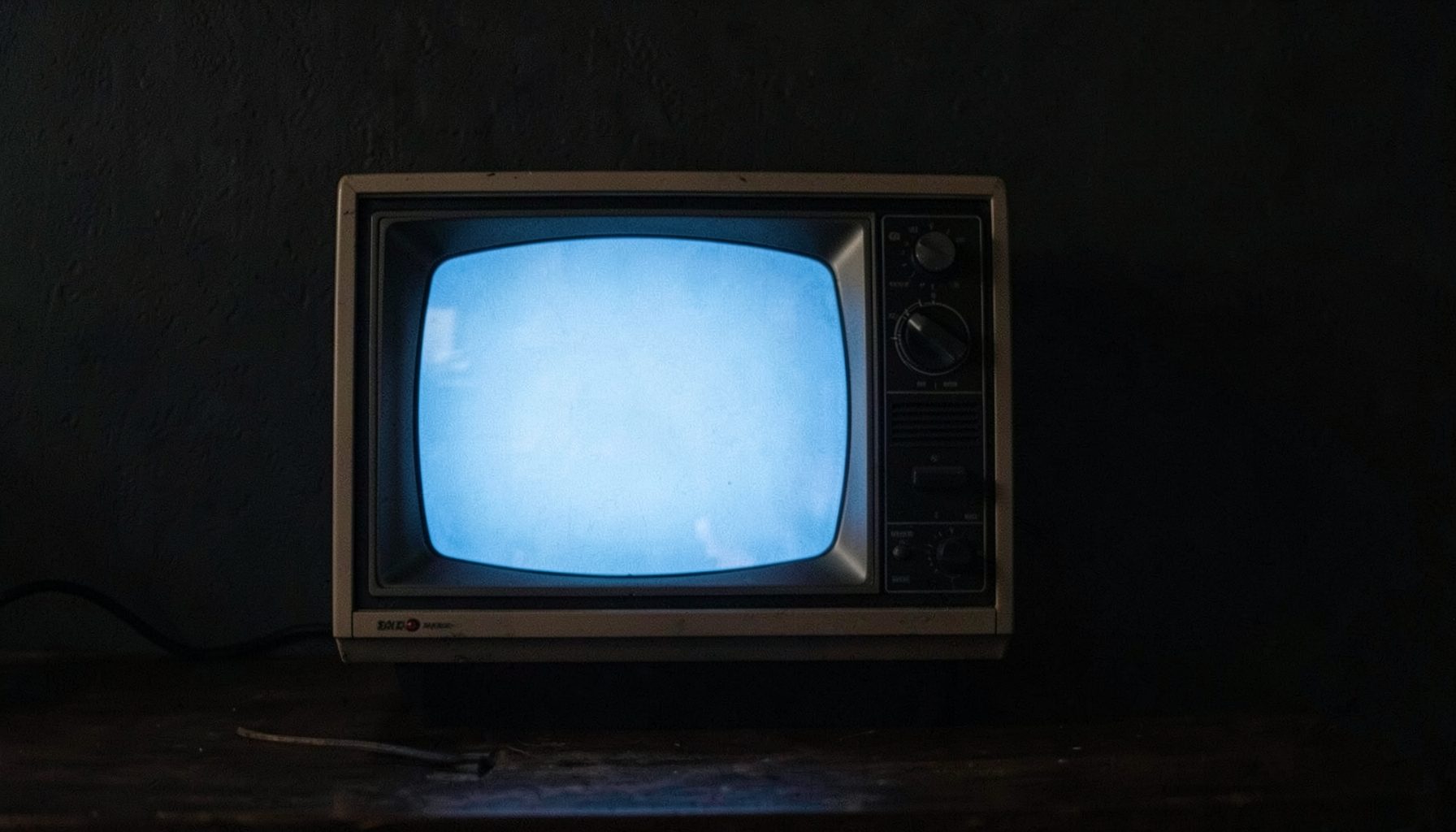 Vintage television set against a dark wall, soft blue glow from the screen, nostalgic mood