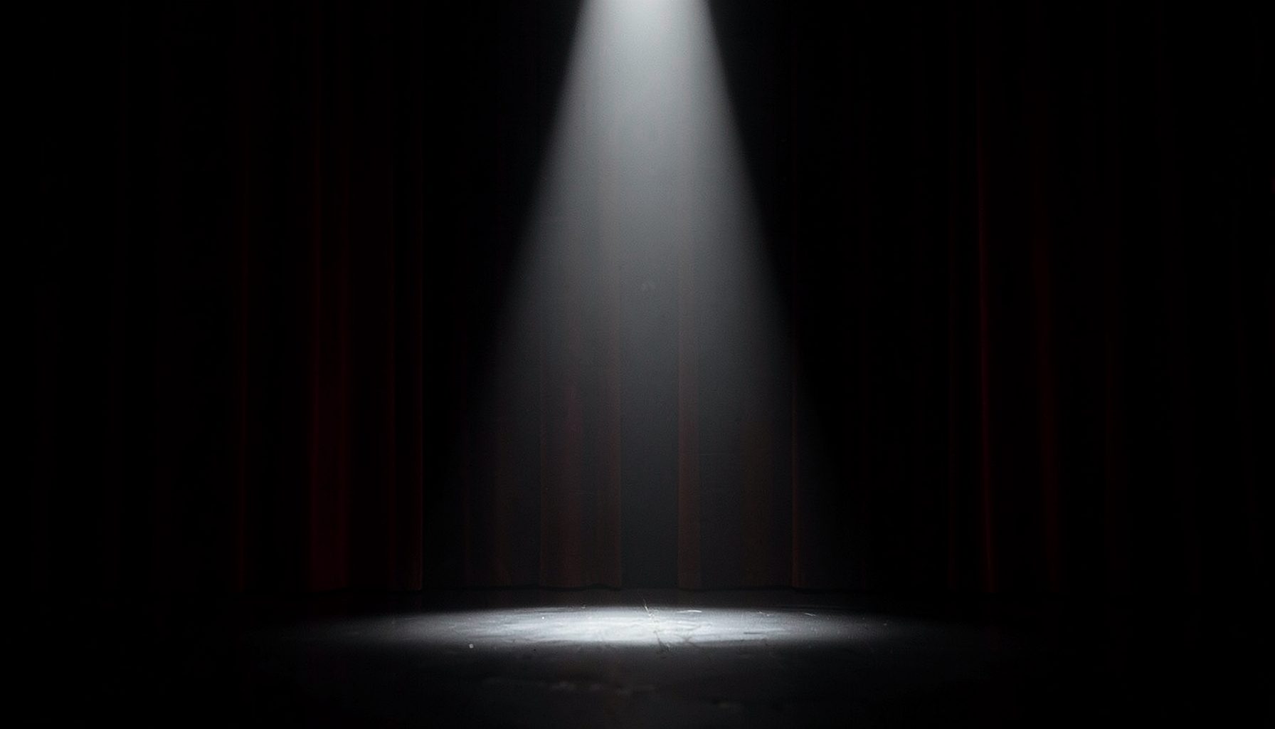 Single spotlight on a dark stage with faint red curtains in the background, dramatic and somber