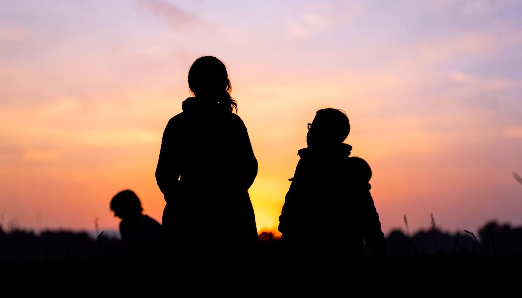 A family silhouette against a warm sunset in soft orange and lavender hues, evoking togetherness