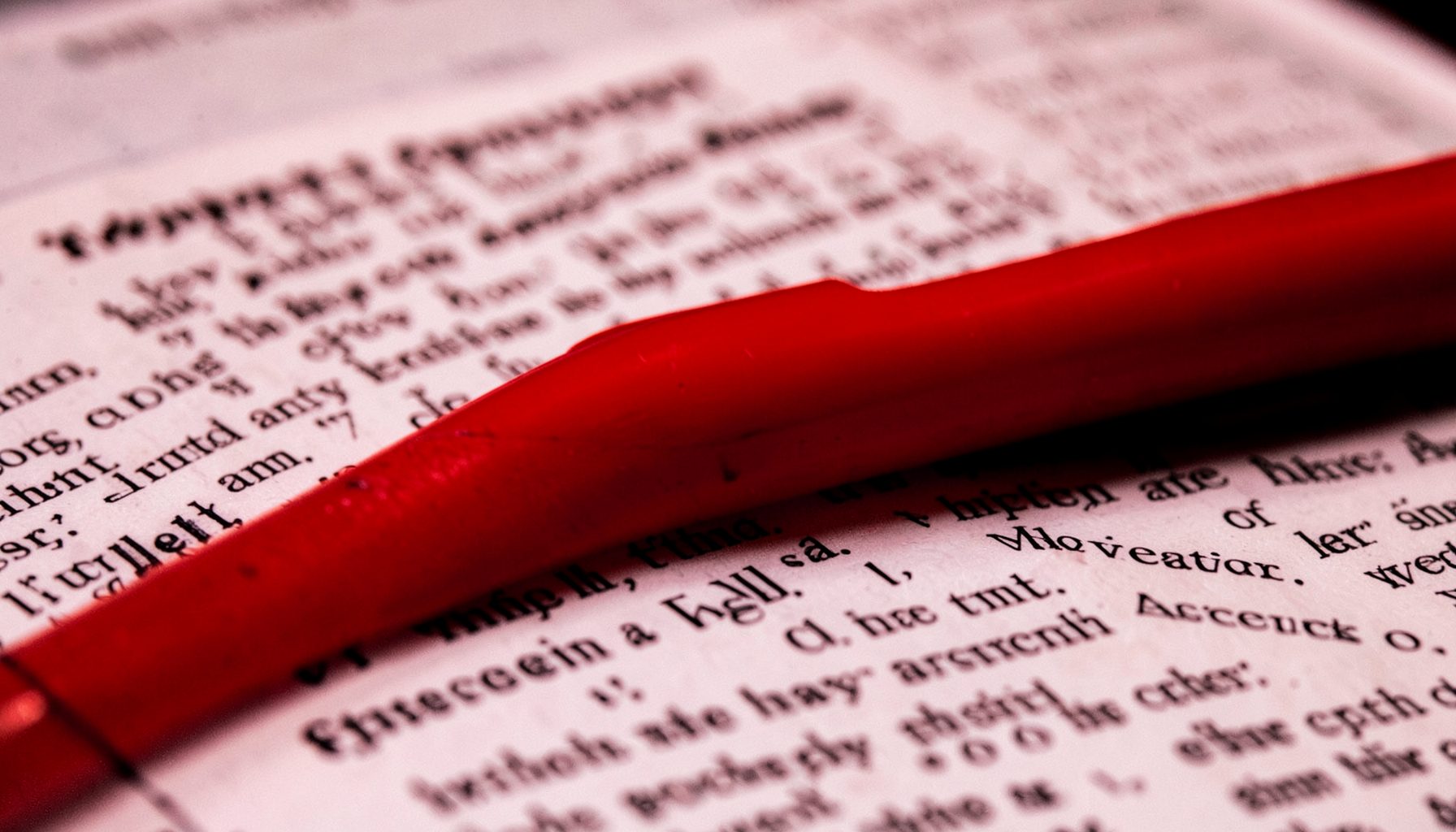 Close-up of a red pen resting on printed headlines in dramatic red and black contrast